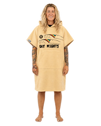 A woman stands barefoot against a plain white studio background wearing a tan hooded towel dress with a 'GAY RIGHTS' graphic on the front.