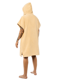 A person shown from the back wearing a light beige hooded towel robe, standing barefoot against a plain white studio background.